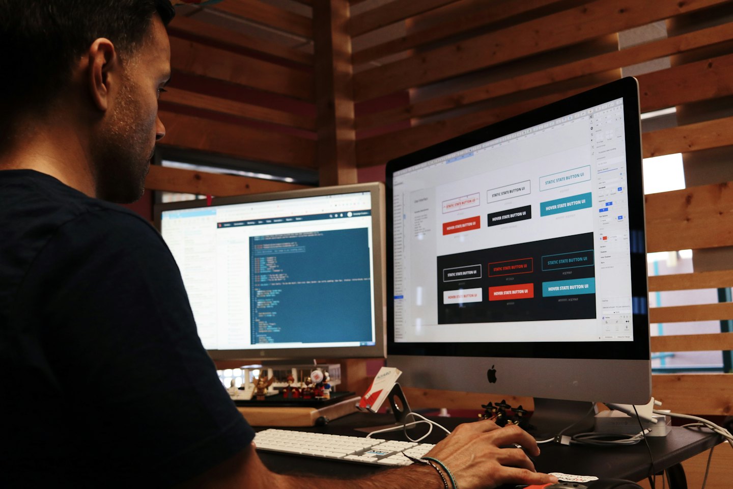 Man designing user interface buttons and coding on dual computer monitors.