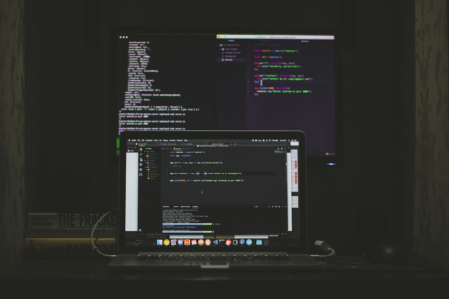 Laptop and external monitor displaying code on a desk.