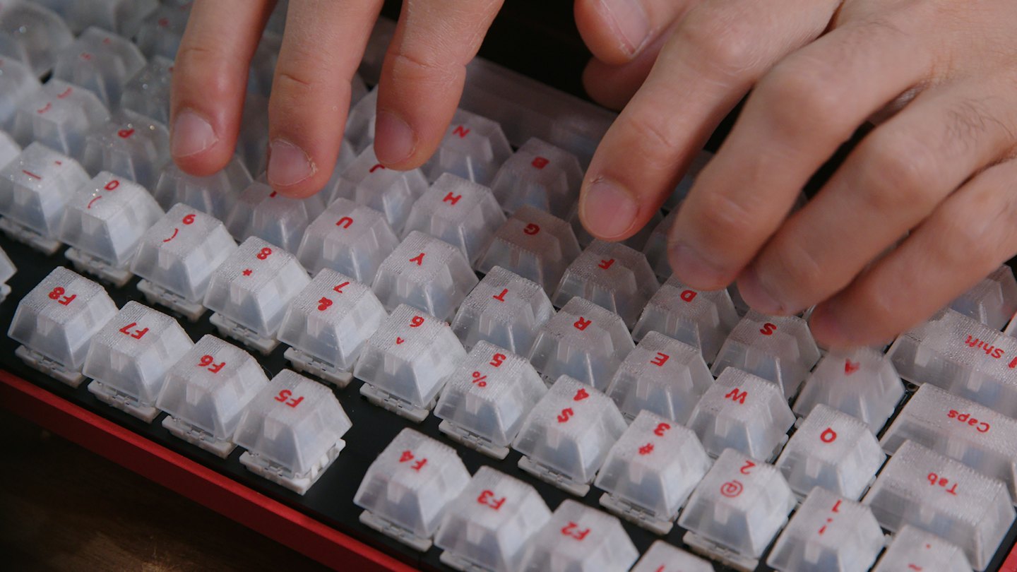 Hands typing on a red and black mechanical keyboard with white keys.